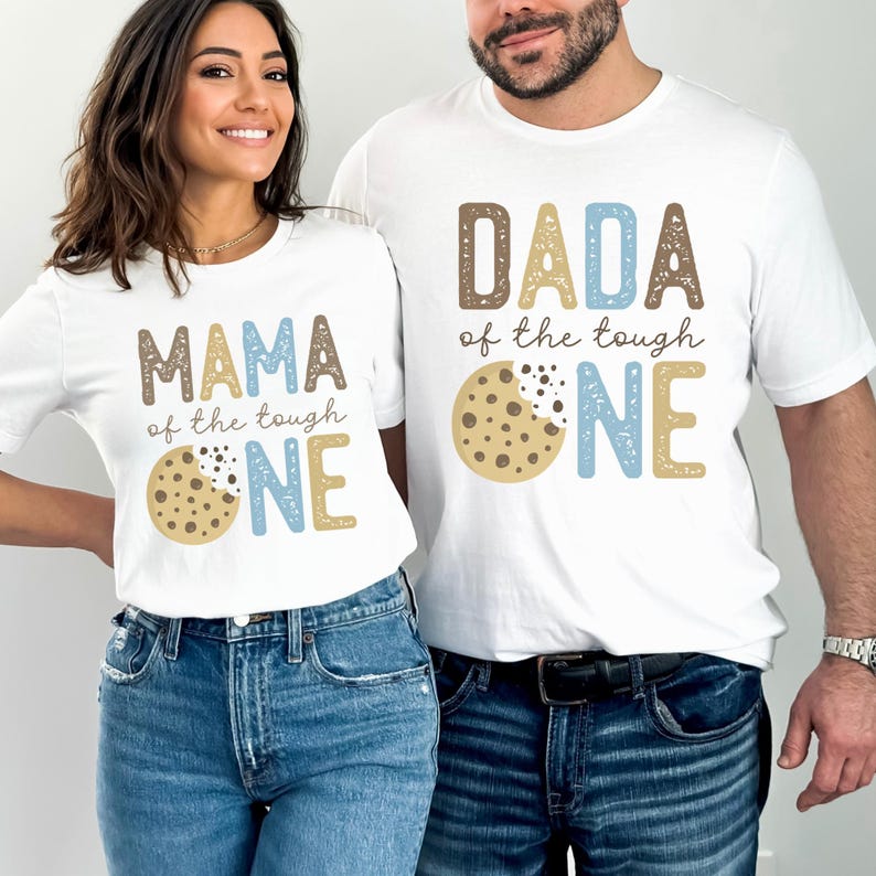 May include: Two white t-shirts with matching designs. One shirt says "MAMA of the tough ONE" and the other says "DADA of the tough ONE". Both shirts feature a cookie graphic. The shirts are worn by two people.