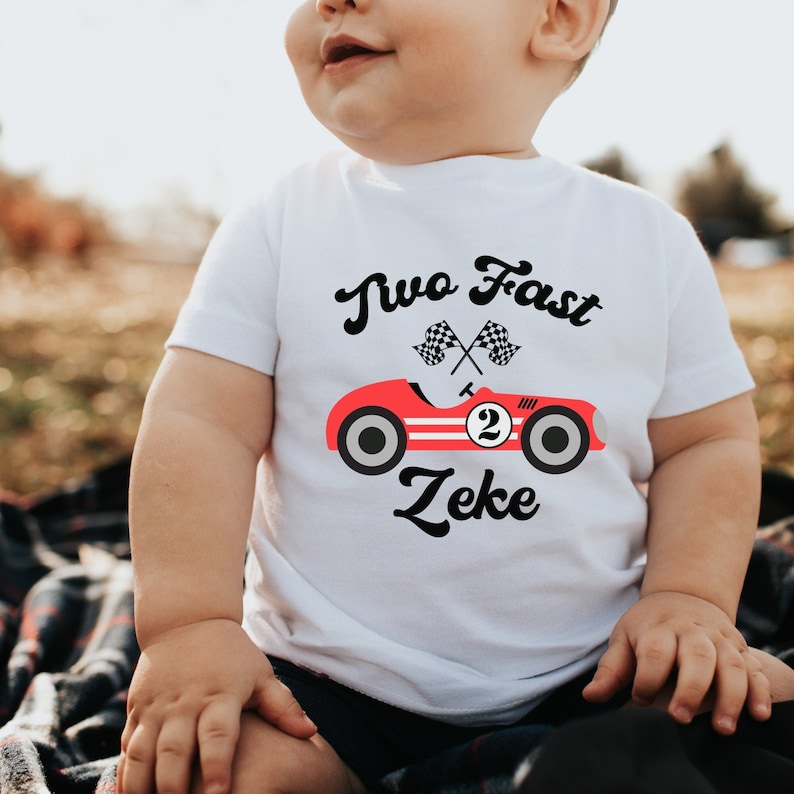 May include: A white short-sleeved shirt with a red race car graphic and the text "Two Fast Zeke".