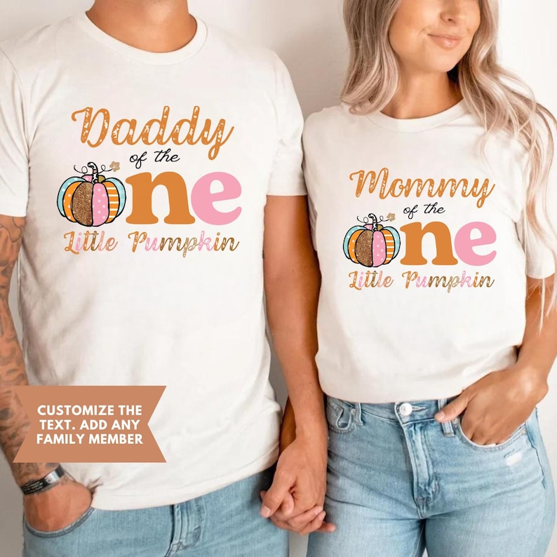 Puede incluir: Dos camisetas blancas con un gr&aacute;fico de calabaza y el texto "Daddy of the One Little Pumpkin" y "Mommy of the One Little Pumpkin".