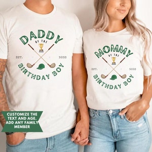 May include: White t-shirts with green text and graphics. The text on the shirts reads "Daddy of the Birthday Boy Est. 2023" and "Mommy of the Birthday Boy Est. 2023". The graphics include crossed golf clubs, a golf ball, and a golf hat.
