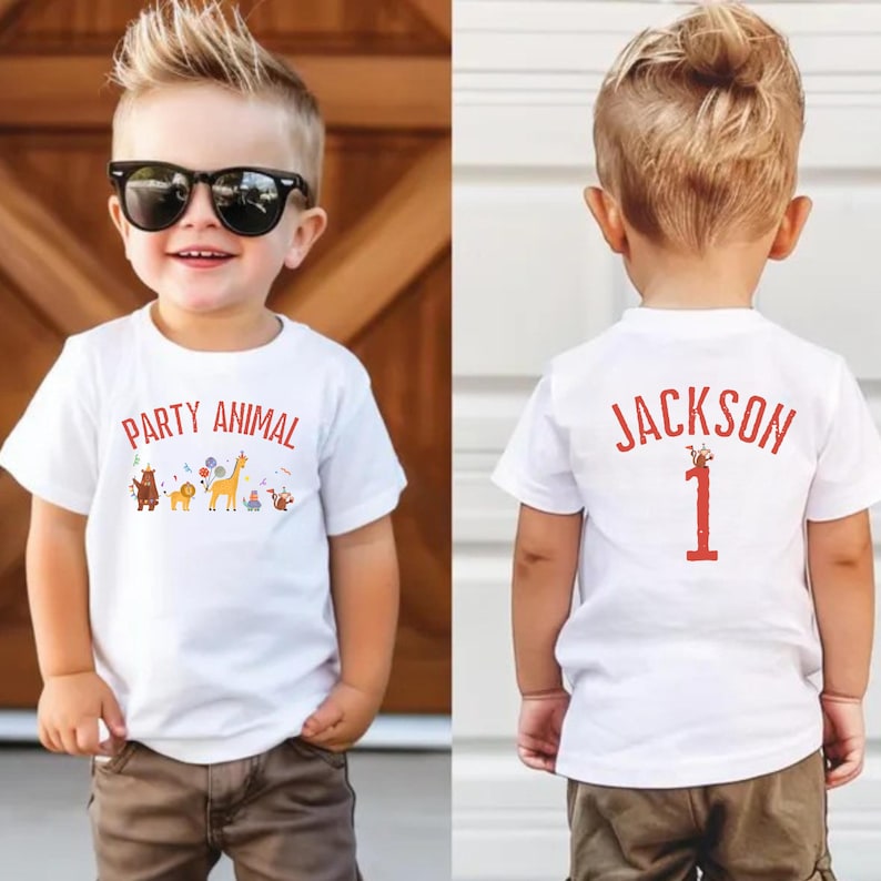 Peut inclure: Un jeune enfant portant un t-shirt blanc avec les mots "PARTY ANIMAL" et un graphisme animalier color&eacute;. L'enfant porte &eacute;galement des lunettes de soleil et un pantalon marron. Le dos du t-shirt porte le nom "JACKSON" et le chiffre "1".