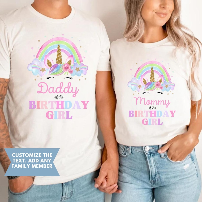K&ouml;nnte beinhalten: Zwei wei&szlig;e T-Shirts mit einem Regenbogen- und Einhorn-Design. Der Text auf den Shirts lautet "Daddy of the Birthday Girl" und "Mommy of the Birthday Girl".