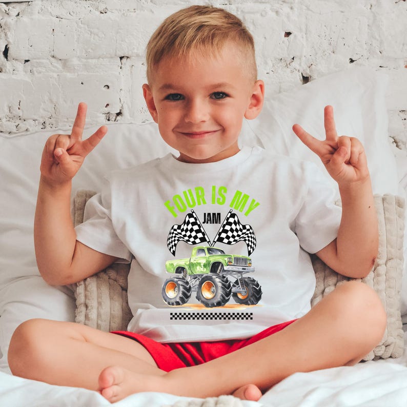 Puede incluir: Camiseta blanca con un gr&aacute;fico de cami&oacute;n monstruo verde y el texto "FOUR IS MY JAM". La camiseta presenta banderas a cuadros y un borde a cuadros en blanco y negro. El ni&ntilde;o lleva pantalones cortos rojos.