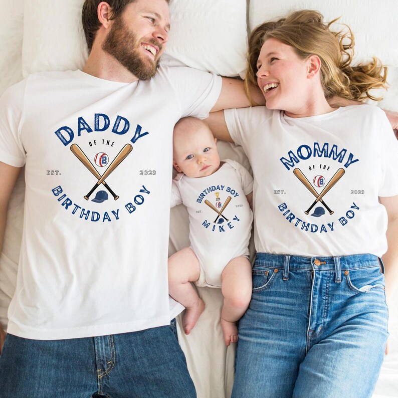 K&ouml;nnte beinhalten: Wei&szlig;e T-Shirts und ein Baby-Body mit Baseball-Motiven. Die Shirts tragen die Aufschrift "Daddy of the Birthday Boy" und "Mommy of the Birthday Boy" mit gekreuzten Schl&auml;gern und einem Baseball. Der Body tr&auml;gt die Aufschrift "Birthday Boy Mikey".