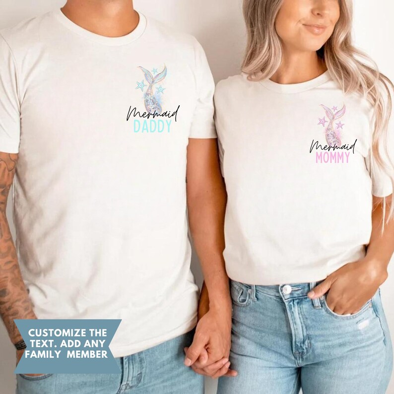 May include: Two off-white t-shirts with mermaid tail and star graphics. One shirt says "Mermaid Daddy" in blue, the other says "Mermaid Mommy" in pink. The shirts are worn by two people. The text "Customize the text. Add any family member" is at the bottom.