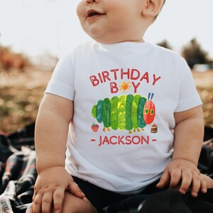 Może przedstawiać: Biała koszulka z kolorową grafiką gąsienicy i napisem "BIRTHDAY BOY - JACKSON" w kolorze czerwonym. Gąsienica jest zielono-ż&oacute;łta z czerwoną głową. Występują r&oacute;wnież truskawka i ciasto.