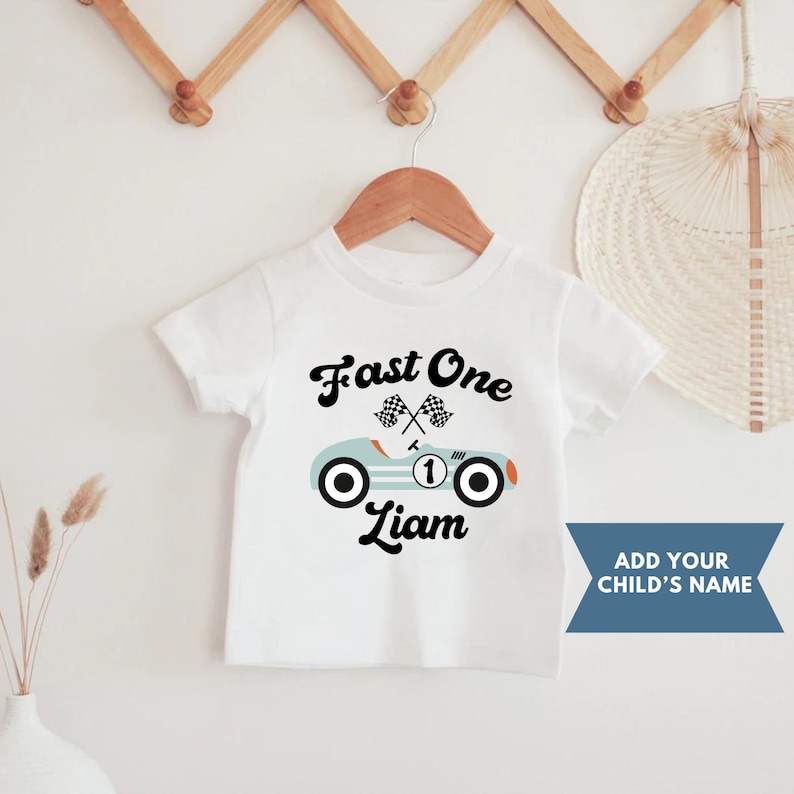 May include: White t-shirt with a blue and orange race car graphic and the text "Fast One" and "Liam".