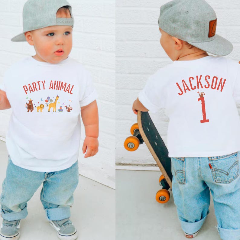Peut inclure: T-shirt blanc avec l'inscription "PARTY ANIMAL" et un motif animalier color&eacute;. Le dos du t-shirt porte le nom "JACKSON" et le chiffre "1" imprim&eacute; en rouge. L'enfant porte un jean bleu et une casquette de baseball grise.