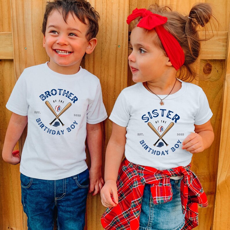 K&ouml;nnte beinhalten: Zwei Kinder tragen wei&szlig;e T-Shirts mit Baseball-Grafiken. Die Shirts tragen die Aufschrift "Bruder des Geburtstagskindes" und "Schwester des Geburtstagskindes" mit gekreuzten Schl&auml;gern, einem Baseball und einer Kappe. Der Junge tr&auml;gt blaue Jeans, und das M&auml;dchen tr&auml;gt ein rot kariertes Hemd.