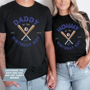 K&ouml;nnte beinhalten: Schwarze T-Shirts mit Baseball-Grafiken. Eines zeigt "DADDY of the BIRTHDAY BOY" mit gekreuzten Schl&auml;gern, einem Baseball und einer Kappe. Das andere zeigt "MOMMY of the BIRTHDAY BOY". Beide haben "EST. 2023".