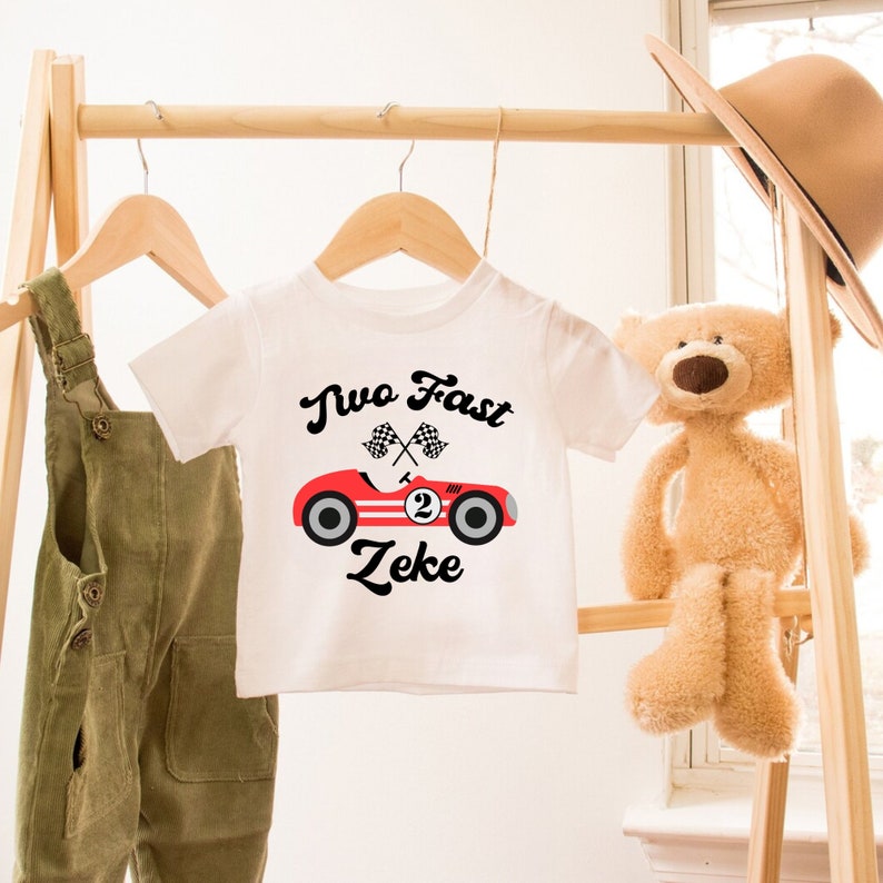 May include: White t-shirt with a red race car graphic and the text "Two Fast Zeke".