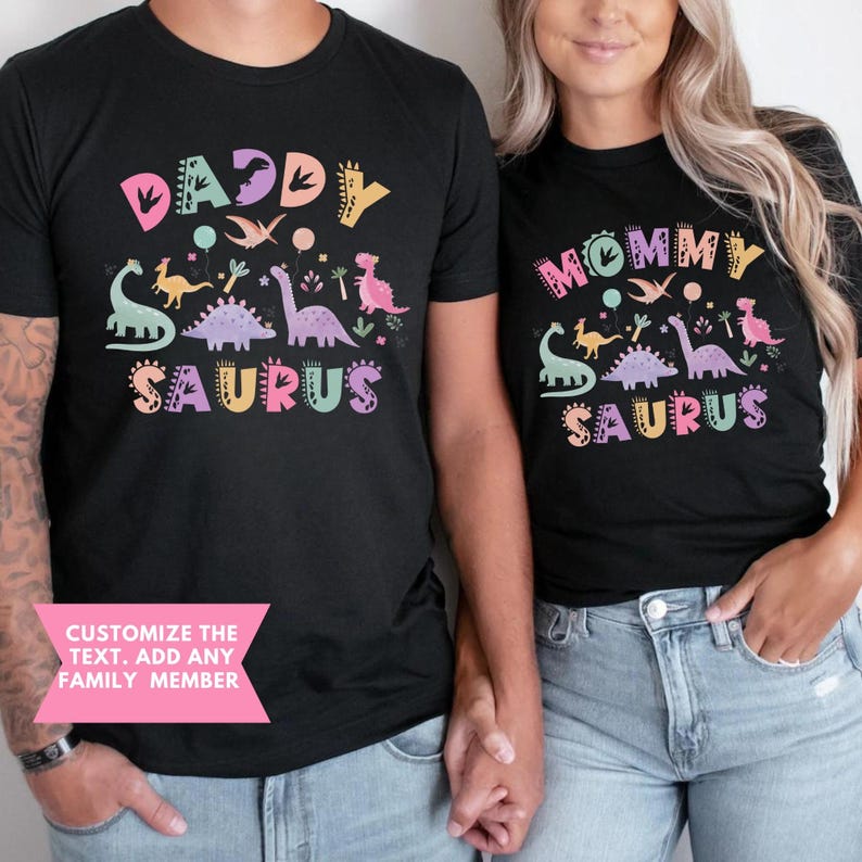 May include: Black t-shirts featuring dinosaur graphics and the phrases "Daddy Saurus" and "Mommy Saurus". The shirts have a playful design with various dinosaur illustrations and the text "Customize the text. Add any family member".