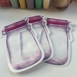 May include: Two clear plastic reusable storage bags with a purple and pink mason jar design. The bags have a zipper closure and are ideal for storing food or other small items.