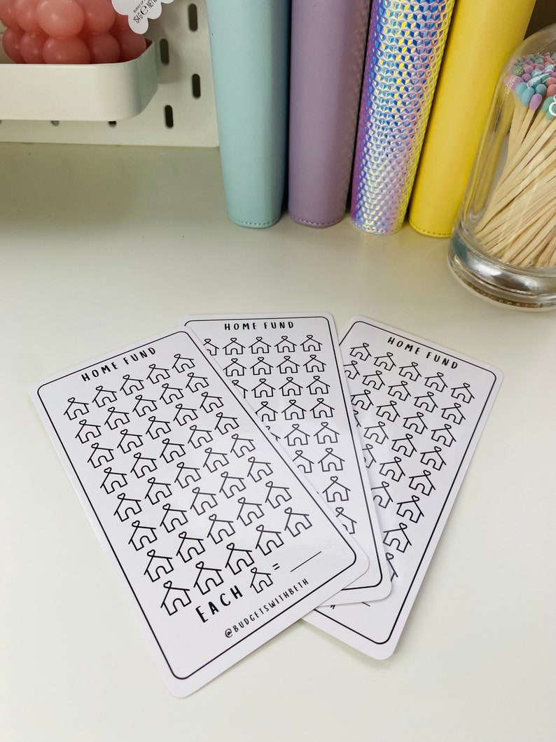 May include: Three white cards with black outlines of houses on them. The cards are labeled "Home Fund" and have the text "Each =" at the bottom. The cards are stacked on top of each other.