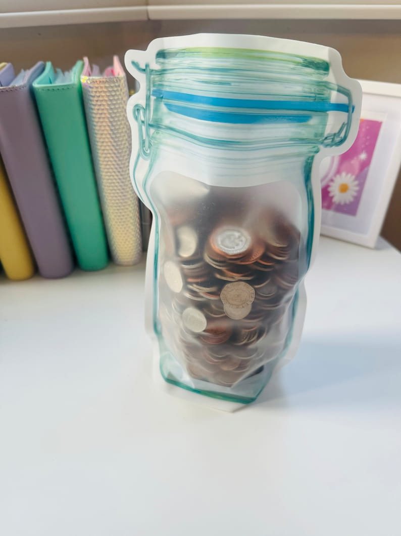 May include: A clear plastic bag shaped like a glass jar filled with a stack of coins. The bag has a blue and green design.