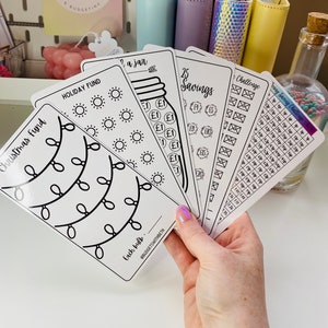 May include: A set of five printable budgeting trackers with black and white designs. The trackers include a Christmas fund, a holiday fund, a savings tracker, a challenge tracker, and a jar tracker. The trackers are designed to help people save money and reach their financial goals.