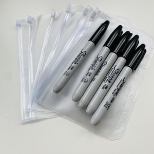May include: A stack of clear plastic zippered pouches with black Sharpie permanent markers. The markers have the text "Sharpie" and "Fine Point" printed on them.