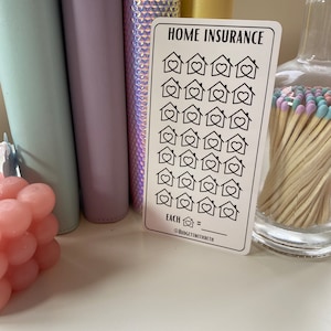 May include: A white card with the text "HOME INSURANCE" printed in black. The card has 25 black and white house icons with hearts inside. The text "EACH  =  " is printed below the icons. The text "@BUDGETSWITHBETH" is printed below the line.