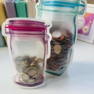 May include: Two clear plastic bags shaped like jars, filled with coins. The bag on the left has a pink lid and the bag on the right has a blue lid.