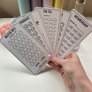May include: A set of six white cards with black outlines and text. The cards are for tracking expenses and include categories like water bill, insurance, car tax, and membership. Each card has a different design and includes a total amount.