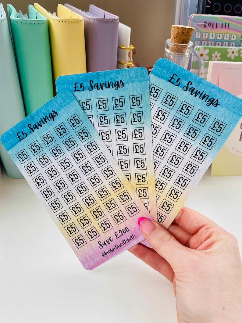 May include: Five colorful cards with a watercolor background. Each card has a grid of squares with the text "&pound;5" written inside each square. The cards are labeled "&pound;5 Savings" and the bottom card has the text "Save &pound;200" and "@budgetswithbeth".