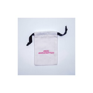 May include: A small, off-white drawstring bag with black drawstrings. The bag has the text "ANGEL HANDICRAFTSCO" printed in pink. The bag is likely used for storing small items like jewellery or gifts.