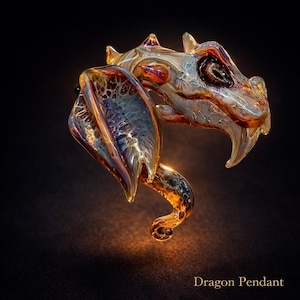 Op de afbeelding: Een gedetailleerde glazen drakenhanger met iriserende kleuren blauw, goud en paars. De kop van de draak is ingewikkeld ontworpen met scherpe tanden en getextureerde schubben. De tekst "Dragon Pendant" staat onderaan.