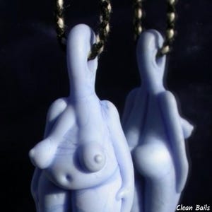 May include: Two light blue pendant necklaces, each featuring a stylized female form. The pendants are suspended from black and white cords. The figures have rounded shapes and are detailed with anatomical features.
