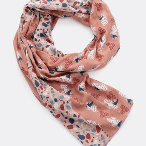Könnte beinhalten: Korallfarbener Schal mit einem sich wiederholenden Muster aus weißen wolkenartigen Formen mit blauen Vögeln und roten floralen Akzenten. Eine Seite zeigt ein Terrazzo-Design mit roten, blauen und beigen Fragmenten. Der Schal ist aus leichtem Stoff.
