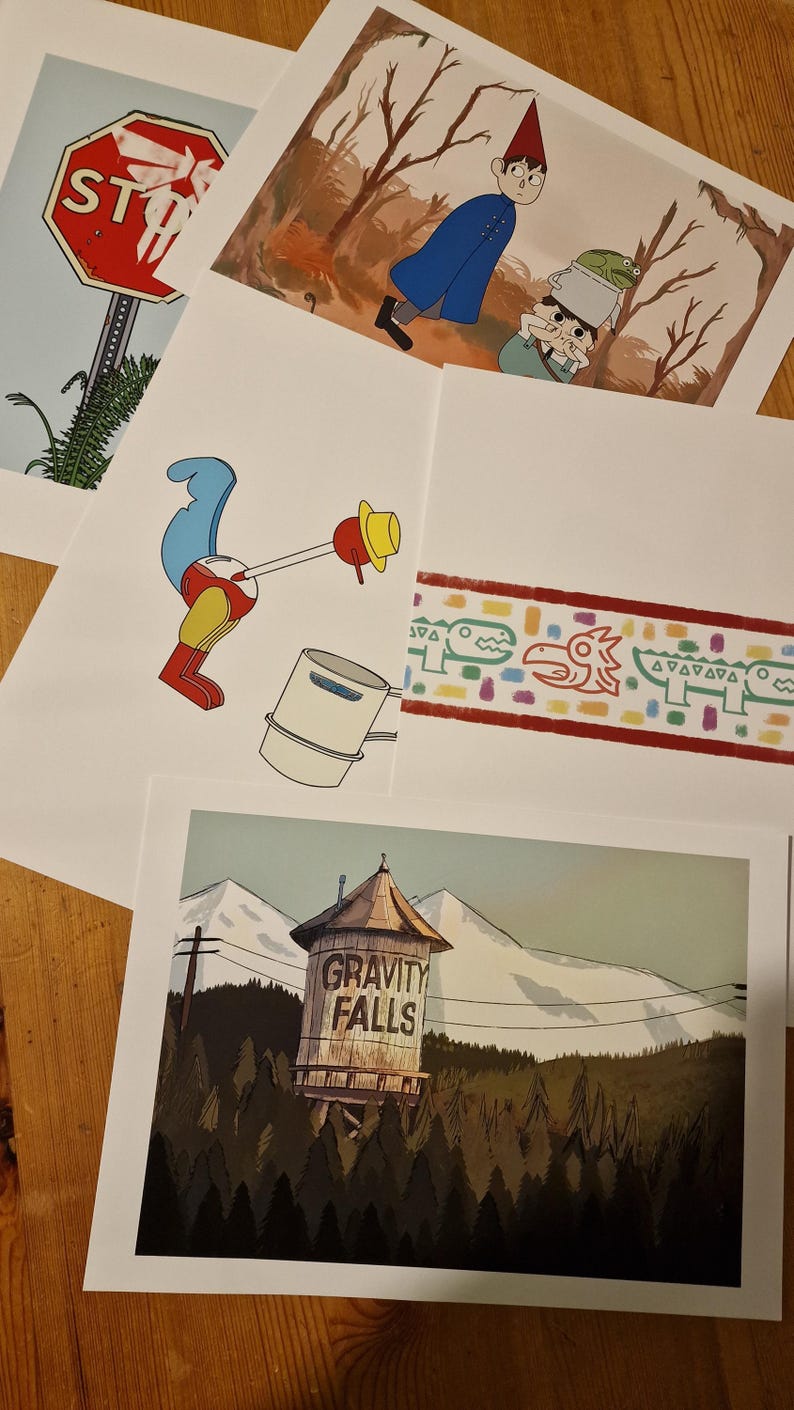 May include: Four different prints featuring characters and imagery from the animated television series Gravity Falls. The prints include a stop sign, a character with a frog on their head, a bird with a bucket, and a water tower with the words "Gravity Falls" on it.