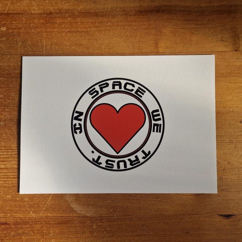 May include: A white card with a black and red circle design. The circle says "In Space We Trust" with a red heart in the center.