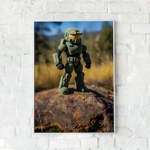 Pode incluir: Uma figura de ação verde e preta do Master Chief está em pé em uma rocha em um campo gramado. A figura está usando um capacete e armadura.