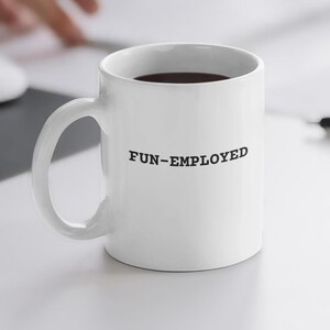 May include: White ceramic coffee mug with a black handle and the text "FUN-EMPLOYED" printed on the front.