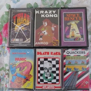 May include: A collection of six vintage video game cartridges for the Commodore VIC-20. The cartridges are in their original packaging and feature colorful graphics and text. The titles include "Triad", "Krazy Kong", "Space Rescue", "Software Panic", "Death Race", and "Quackers".