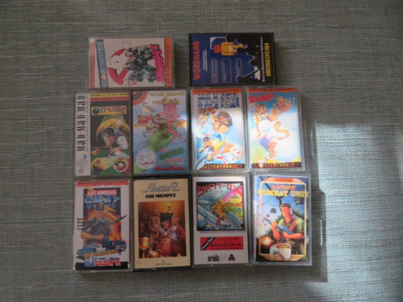 May include: A collection of 10 vintage video game cartridges for the Amstrad CPC computer. The cartridges are in clear plastic cases with colorful artwork featuring characters and scenes from the games. The titles include "Mad Mad Mad", "Los Angeles SWAT", "Skyfox", "Saigon Combat Unit", "Bump", "Milk Race", "Vent D'mar", "Your Head", "Phaser", and "Wordhang".