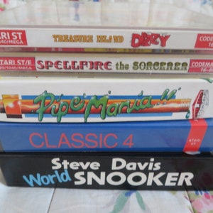 Puede incluir: Una pila de cinco cartuchos de videojuegos para la computadora Atari ST. Los cartuchos están etiquetados como "Treasure Island Dizzy", "Spellfire the Sorcerer", "Pipe Mania", "Classic 4" y "Steve Davis World Snooker".