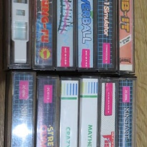 May include: A collection of 10 vintage video game cartridges for the Commodore 64. The cartridges are in various colors and have titles such as "Powerball", "Formula 1 Simulator", "Climb-It", "Kickstart", "Fist", "Mayhem", "Crazy Golf", "Street  Olympics", and "W.I.N."