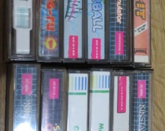 Può includere: Una collezione di 10 cartucce di videogiochi vintage per Commodore 64. Le cartucce sono di vari colori e hanno titoli come "Powerball", "Formula 1 Simulator", "Climb-It", "Kickstart", "Fist", "Mayhem", "Crazy Golf", "Street  Olympics" e "W.I.N."