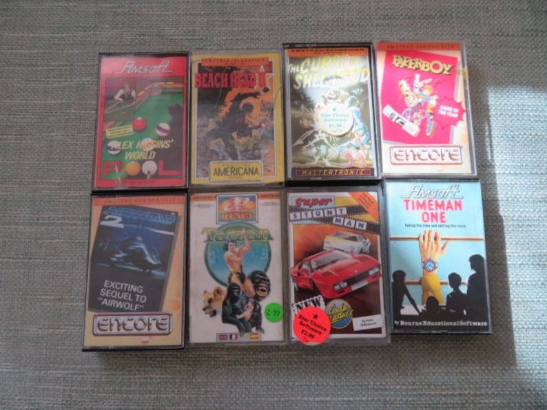 May include: Eight vintage cassette tapes for a video game console. The tapes are in various colors and feature different game titles, including "Alex Higgins' World", "Beach Head", "The Chuckle Brothers Show", "Paperboy", "Airwolf 2", "Zzap! Test Drive", "Super Stuntman", and "Timeman One".