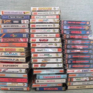 May include: A stack of vintage video game cartridges for the ZX Spectrum home computer. The cartridges are arranged in two columns, with titles such as "Bronx Street Cop", "Harrier Attack", "Super", "Mini Office", "Cobra", "Wonder Boy", "Tarzan", "Airwolf 2", "Paperboy", "Timeman One", "Skyfox", "Bump'n'Jump", and "Wordhang".