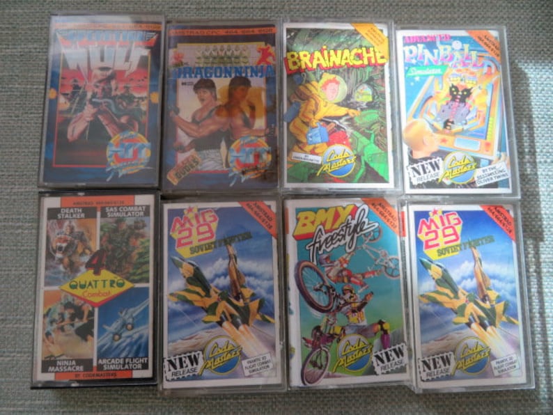 May include: A collection of 10 vintage video game cartridges for the Commodore 64. The cartridges are arranged in two rows of five. The cartridges are all in their original packaging and are in good condition. The cartridges include games such as Wolf, Dragon Ninja, Brainace, Pinball, Death Stalker, SAS Combat Simulator, Quattro Combat, MIG 29 Soviet Fighter, BMX Freestyle, and MIG 29 Soviet Fighter.