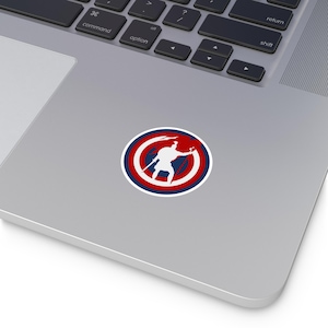 May include: A white silhouette of a person holding a spear stands in the center of a red, white, and blue circle. The circle has a star in the center and is reminiscent of the American flag.