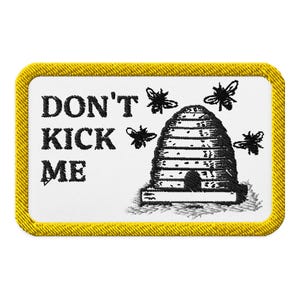 Könnte beinhalten: Gestickter Aufnäher mit weißem Hintergrund und gelbem Rand. Der Aufnäher zeigt einen schwarzen Bienenstock mit vier schwarzen Bienen und dem Text "DON'T KICK ME" in Schwarz.