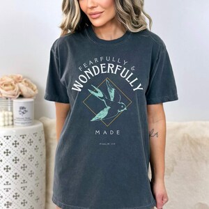 May include: A dark gray t-shirt with a white graphic that says "Fearfully & Wonderfully Made" with a small bird design and the text "Psalm 139".