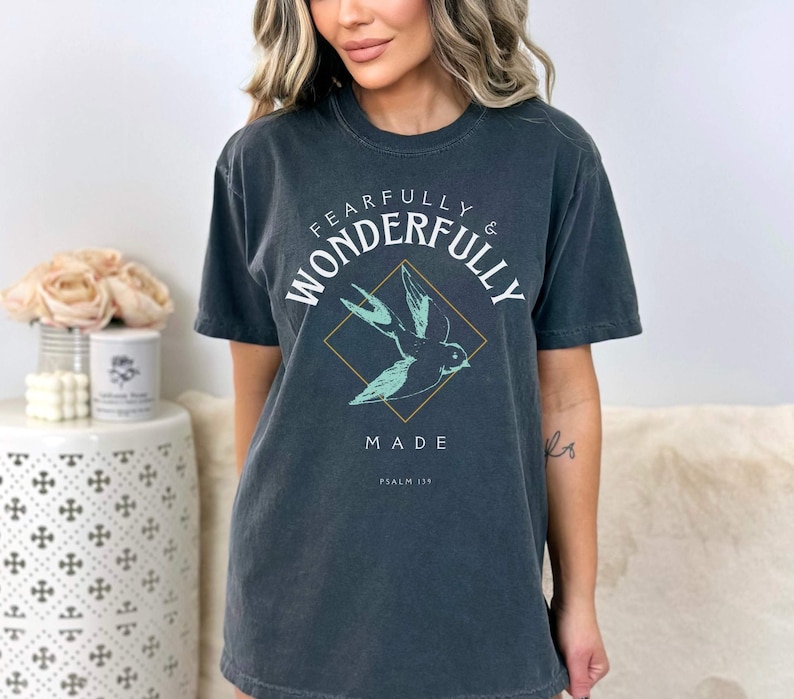 May include: A dark gray t-shirt with a white graphic that says "Fearfully & Wonderfully Made" with a small bird design and the text "Psalm 139".