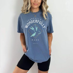 May include: A blue oversized t-shirt with a white graphic of a bird in a diamond shape. The graphic says "Fearfully & Wonderfully Made" and "Psalm 139".