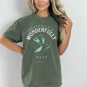 May include: A green t-shirt with a white graphic of a bird in a diamond shape. The text "Fearfully & Wonderfully Made" is written around the diamond. The text "Psalm 139" is written below the diamond.