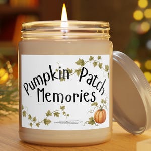 May include: A lit candle in a clear glass jar with a silver lid. The white label features the text 'Pumpkin Patch Memories' in black script, decorated with green vine illustrations and a small orange pumpkin graphic at the bottom right.