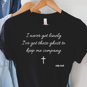 May include: Black t-shirt with white text that reads "I never get lonely I've got these ghost to keep me company" and a white cross. The text "Jelly Roll" is printed below the cross.