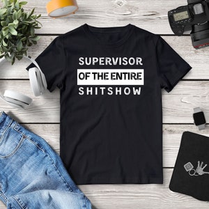 May include: Black t-shirt with white text that reads "SUPERVISOR OF THE ENTIRE SHITSHOW".